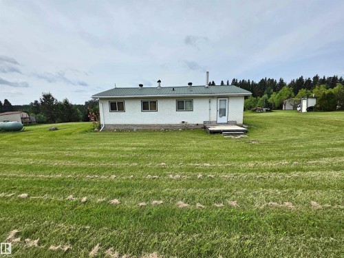 Expansive green space with mature perimeter trees, featuring a white exterior structure with a green metal roof and multiple windows - Rural St. Paul County, AB 