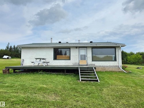White textured exterior with a green roof, featuring a wood-finish deck, exterior steps, and large windows - Rural St. Paul County, AB 