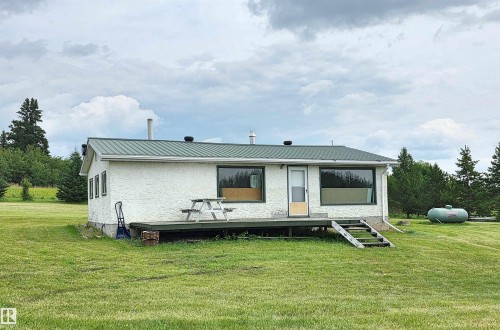 White stucco exterior with a green metal roof and a wood deck - Rural St. Paul County, AB 