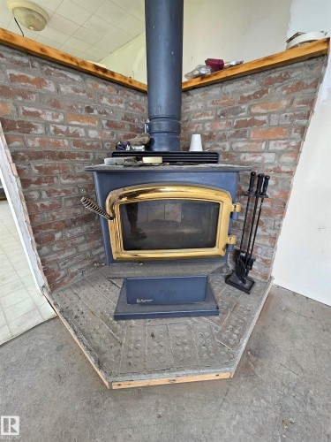 Wood-burning stove with a gold-tone trim, brick surround, and a metal flue - Rural St. Paul County, AB 