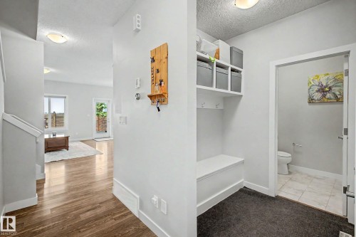 Entryway featuring wood-finish flooring, white trim, built-in storage bench, and an adjacent powder room with tile flooring - 1783 Keene Crescent Sw, Edmonton, AB - Indoor Photo Showing Other Room
