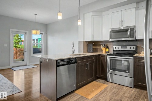 Kitchen featuring stainless steel appliances, wood-finish flooring, two-tone cabinetry, and a granite countertop island with an integrated sink - 1783 Keene Crescent Sw, Edmonton, AB - Indoor Photo Showing Kitchen With Upgraded Kitchen