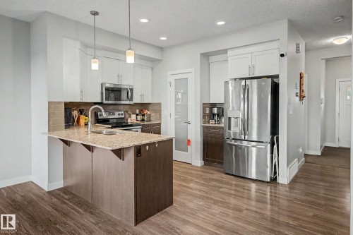 Kitchen featuring wood-finish flooring, two-tone cabinetry, stainless steel appliances, a center island with a stone countertop, and pendant lighting - 1783 Keene Crescent Sw, Edmonton, AB - Indoor Photo Showing Kitchen With Upgraded Kitchen