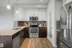 Kitchen featuring granite countertops, stainless steel appliances, two-tone cabinetry, and wood-finish flooring - 