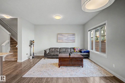 Spacious room featuring wood-finish flooring, a large window, a built-in staircase, and light wall finishes - 1783 Keene Crescent Sw, Edmonton, AB - Indoor Photo Showing Living Room