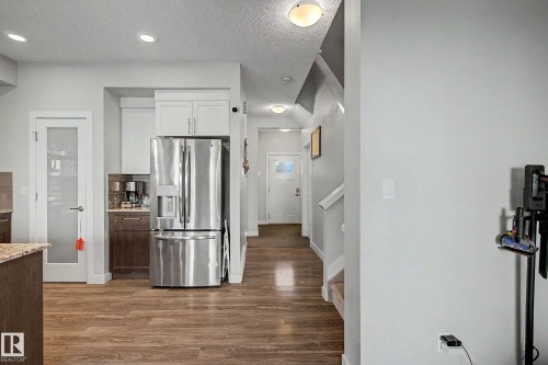 Stainless steel refrigerator, wood-finish flooring, white cabinetry, recessed lighting, and a frosted glass panel door - 1783 Keene Crescent Sw, Edmonton, AB - Indoor