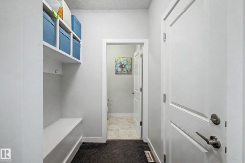 Efficient mudroom entry featuring built-in cubbies with blue-toned storage boxes, a bench seat with integrated shelving, white shaker-style cabinetry, and direct access to a tiled bathroom - 1783 Keene Crescent Sw, Edmonton, AB - Indoor Photo Showing Other Room