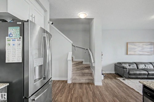 Wood-finish flooring, stainless steel French door refrigerator with ice/water dispenser, white upper cabinetry, and carpeted stairs with white railing - 1783 Keene Crescent Sw, Edmonton, AB - Indoor Photo Showing Other Room