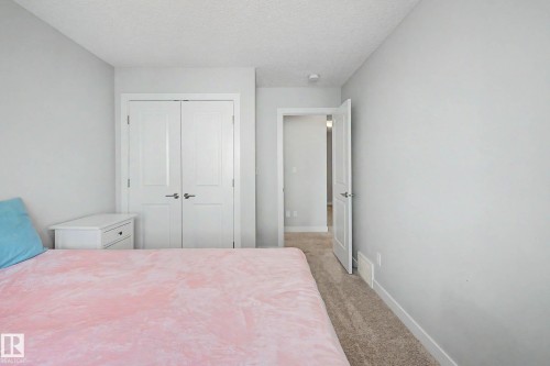 Bright secondary bedroom featuring neutral wall finishes, carpeted flooring, double closet doors with white frames, and a single nightstand with storage - 1783 Keene Crescent Sw, Edmonton, AB - Indoor Photo Showing Bedroom