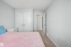 Bright secondary bedroom featuring neutral wall finishes, carpeted flooring, double closet doors with white frames, and a single nightstand with storage - 
