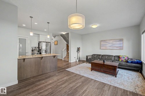 Open-concept living space featuring wood-finish flooring throughout, a custom island with wood cabinetry and stainless steel appliances, pendant lighting, and a spacious seating area anchored by a wood coffee table - 1783 Keene Crescent Sw, Edmonton, AB - Indoor Photo Showing Living Room