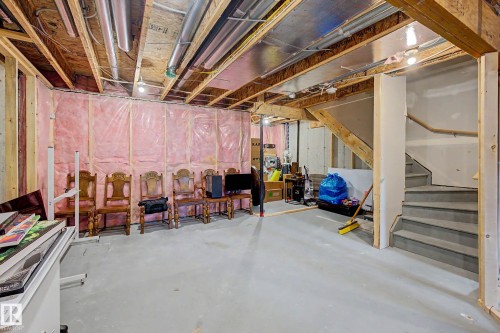 Unfinished basement with exposed ceiling joists and structural beams, insulated walls, concrete flooring, and a staircase with a wooden handrail - 1783 Keene Crescent Sw, Edmonton, AB - Indoor Photo Showing Basement
