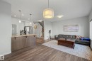 Open-concept living space featuring wood-finish flooring throughout, a custom island with wood cabinetry and stainless steel appliances, pendant lighting, and a spacious seating area anchored by a wood coffee table - 1783 Keene Crescent Sw, Edmonton, AB 