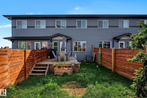 Rear exterior featuring gray horizontal siding, multiple windows, a ground-level wood deck with steps, a raised planter, and privacy fencing - 1783 Keene Crescent Sw, Edmonton, AB - Outdoor