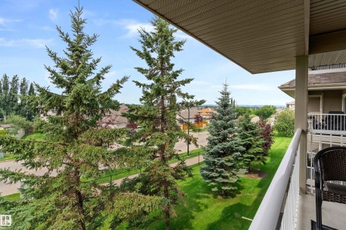 Expansive outdoor space showcasing mature coniferous trees, manicured lawn, and multi-level residential architecture with covered balconies - #305A 6 Spruce Ridge Dr, Spruce Grove, AB - Outdoor With Balcony
