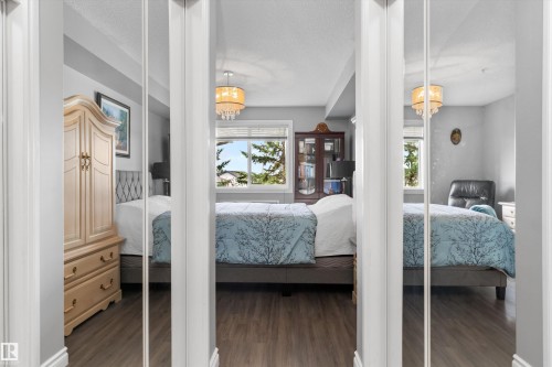 Primary Bedroom Suite with Mirrored Closet Doors and Wood-Finish Flooring  This generously proportioned bedroom features triple mirrored closet doors that amplify natural light throughout the space - #305A 6 Spruce Ridge Dr, Spruce Grove, AB - Indoor