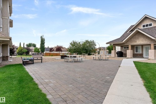 Expansive hardscape patio featuring interlocking pavers, bordered by manicured lawns and mature landscaping - #305A 6 Spruce Ridge Dr, Spruce Grove, AB - Outdoor