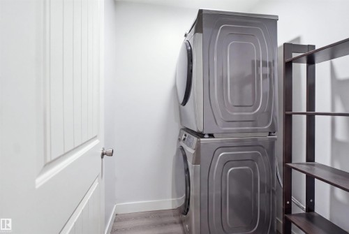 Dedicated laundry area featuring a stacked washer and dryer, wood-finish flooring, and built-in shelving - 714 87 Street Sw, Edmonton, AB - Indoor Photo Showing Laundry Room
