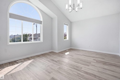 Vaulted ceiling room featuring a large arched window, wood-finish flooring, and a contemporary chandelier - 714 87 Street Sw, Edmonton, AB - Indoor Photo Showing Other Room