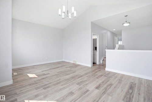 Vaulted ceilings complement wood-finish flooring in this open living area, featuring a contemporary chandelier and a half-wall partition - 714 87 Street Sw, Edmonton, AB - Indoor Photo Showing Other Room