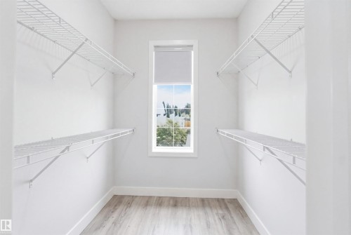 Walk-in closet featuring light wood-finish flooring, white wire shelving, a window with a roller shade, and white baseboards - 714 87 Street Sw, Edmonton, AB - Indoor With Storage