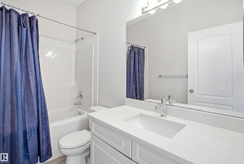 Bathroom featuring a white vanity with an integrated sink and chrome faucet, a large wall-mounted mirror, and overhead vanity lighting - 714 87 Street Sw, Edmonton, AB - Indoor Photo Showing Bathroom
