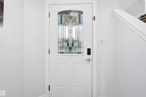 White entry door featuring an arched stained glass insert, a smart lock system, and brushed nickel hardware - 714 87 Street Sw, Edmonton, AB - Indoor Photo Showing Other Room