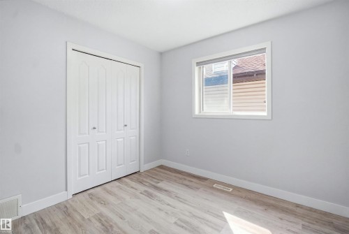 Room featuring wood-finish flooring, a double bi-fold closet, and a white framed window - 714 87 Street Sw, Edmonton, AB - Indoor Photo Showing Other Room