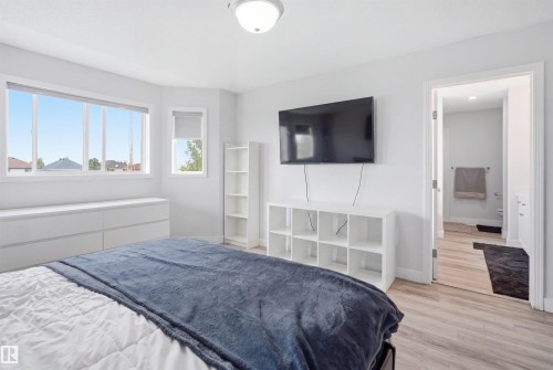 Bright bedroom featuring a large multi-pane window, an additional window with a roller shade, and wood-finish flooring - 714 87 Street Sw, Edmonton, AB - Indoor Photo Showing Bedroom