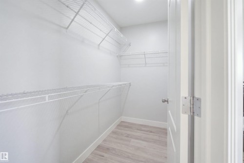 Walk-in closet featuring light wood-finish flooring, white wire shelving, and a bright overhead light fixture - 714 87 Street Sw, Edmonton, AB - Indoor With Storage