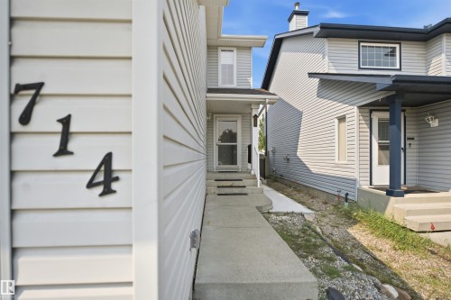 Front exterior featuring light-colored horizontal siding, a concrete walkway, and a dark-framed entryway with a storm door - 714 87 Street Sw, Edmonton, AB - Outdoor