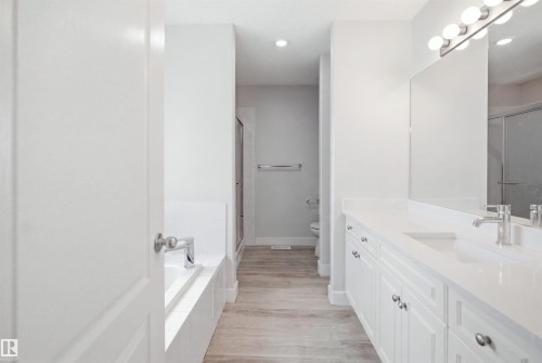 Contemporary bathroom featuring a double vanity with white cabinetry, polished chrome hardware, and a large wall-mounted mirror - 714 87 Street Sw, Edmonton, AB - Indoor Photo Showing Bathroom