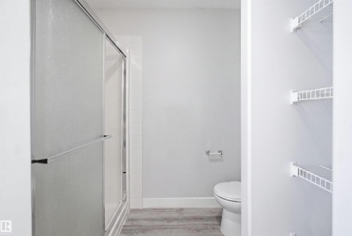 Bathroom featuring a shower with a sliding frosted glass door, a toilet, and wood-finish flooring - 714 87 Street Sw, Edmonton, AB - Indoor Photo Showing Bathroom
