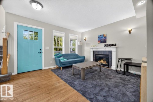 Welcoming foyer with turquoise entry door featuring transom window, wide-plank wood-finish flooring throughout, and abundant natural light from multi-pane glass doors - 887 Oakland Boulevard, Devon, AB - Indoor Photo Showing Living Room With Fireplace