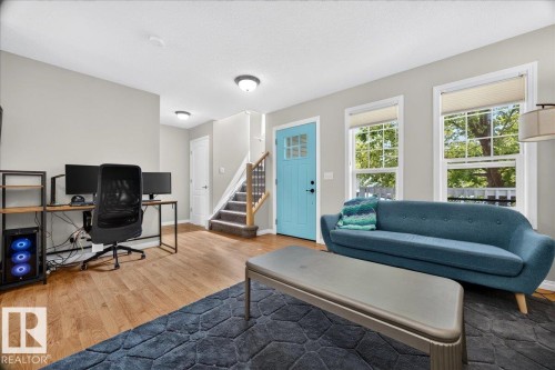 Bright, open living space featuring hardwood flooring, abundant natural light from multiple large windows, a blue upholstered sofa, and a dedicated workspace with built-in desk and shelving - 887 Oakland Boulevard, Devon, AB - Indoor Photo Showing Living Room