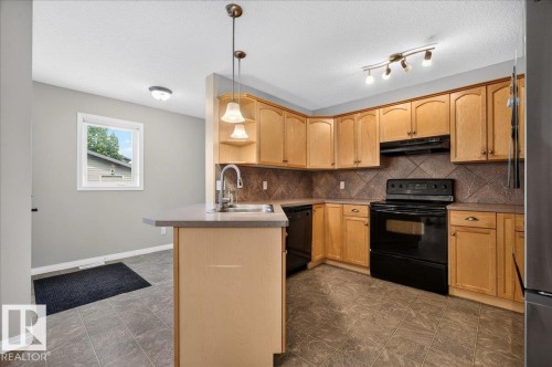 Spacious kitchen featuring warm wood cabinetry, black stainless steel appliances, tile countertops, and a central island with pendant lighting - 887 Oakland Boulevard, Devon, AB - Indoor Photo Showing Kitchen With Double Sink