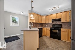 Spacious kitchen featuring warm wood cabinetry, black stainless steel appliances, tile countertops, and a central island with pendant lighting - 