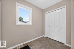 Bright secondary bedroom featuring neutral taupe walls, a large double-door closet with six-panel white doors, and a picture window allowing natural light - 
