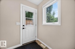 Bright entryway with white six-panel entry door featuring dual handles and glass insert, large casement window with white trim flooding the space with natural light, and dark tile flooring - 