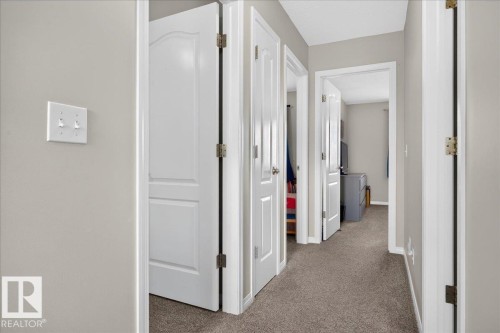 Hallway featuring multiple white six-panel doors with oil-rubbed bronze hardware, neutral wall finishes, and neutral-toned carpet flooring throughout - 887 Oakland Boulevard, Devon, AB - Indoor Photo Showing Other Room