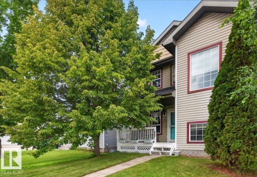 Two-story residence featuring horizontal siding exterior with a covered front porch, decorative railings, and an arched entryway - 887 Oakland Boulevard, Devon, AB - Outdoor