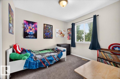 Bright secondary bedroom featuring carpeted flooring, large windows with blackout curtains, white bed frame, wood-finish desk, and colorful wall art - 887 Oakland Boulevard, Devon, AB - Indoor Photo Showing Bedroom