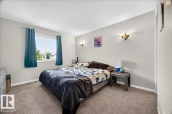 Spacious primary bedroom featuring neutral wall finishes, carpeted flooring, dual nightstands with integrated lighting, and large windows with thermal-lined drapery - 