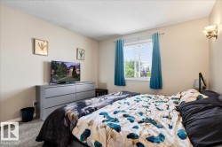 Comfortable bedroom featuring carpet flooring, a gray dresser with built-in storage, wall-mounted television, and large window with blue curtains allowing natural light into the space - 