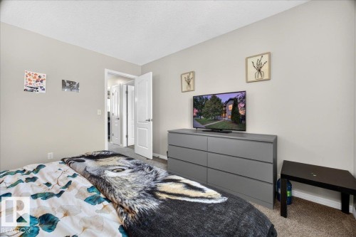 Bright secondary bedroom featuring neutral wall finishes, carpeted flooring, and a large dresser with integrated television mount - 887 Oakland Boulevard, Devon, AB - Indoor Photo Showing Bedroom