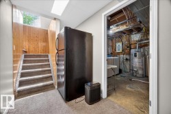 Utility hallway featuring wood-finish stairs with metal railings, carpeted flooring, skylight above, and direct access to mechanical room with visible HVAC systems and water heater - 