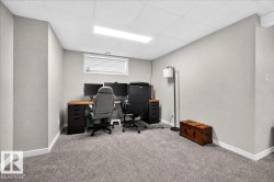 Dedicated home office featuring dual wood-finish desks with ample workspace, comfortable ergonomic seating, recessed ceiling lighting, carpeted flooring, and a high-set window with blinds for natural light and privacy - 