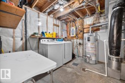 Utility space featuring washer and dryer appliances, concrete flooring, exposed wood-beam ceiling, ductwork infrastructure, and shelving for storage and supplies - 