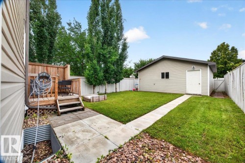 Spacious backyard featuring a manicured lawn, mature poplar trees, concrete walkway, detached storage shed, and defined planting beds with decorative rock landscaping - 887 Oakland Boulevard, Devon, AB - Outdoor
