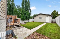 Spacious backyard featuring a manicured lawn, mature poplar trees, concrete walkway, detached storage shed, and defined planting beds with decorative rock landscaping - 